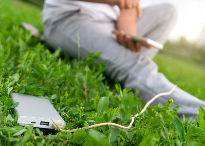 Powerbank ładuje smartfon podczas odpoczynku użytkownika na świeżym powietrzu